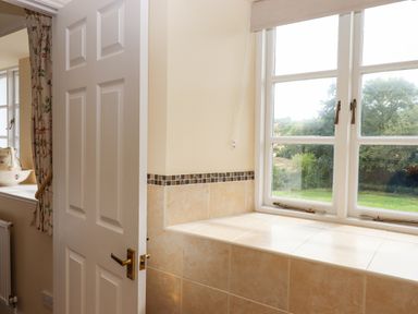 A room with a partially open white door tiles under a window with a view of greenery at Culver Court Cottage in Venny Tedburn near Crediton