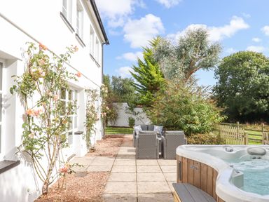 An outdoor patio area with a hot tub and seating near a white building with climbing plants at Culver Court Cottage in Venny Tedburn near Crediton