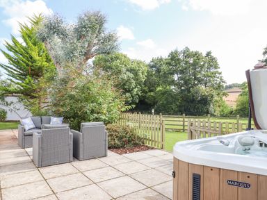 A patio with gray outdoor chairs and a hot tub next to a wooden fence and garden at Culver Court Cottage Venny Tedburn near Crediton
