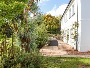 An outdoor patio area with a seating arrangement next to a white building with climbing plants at Culver Court Cottage in Venny Tedburn near Crediton