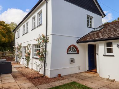 The exterior of a white two story house with multiple windows a blue door and climbing roses on the wall at Culver Court Cottage in Venny Tedburn near Crediton