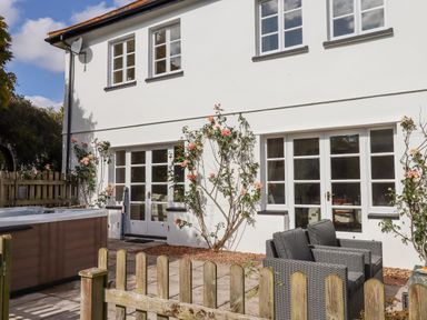 A patio with outdoor chairs hot tub and climbing roses on the wall of a white two-story house at Culver Court Cottage Venny Tedburn near Crediton