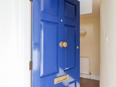 A partially open blue front door showing an entryway with a radiator and beige walls at Culver Court Cottage in Venny Tedburn near Crediton