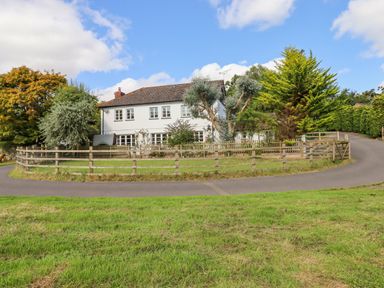 A two-story house with multiple windows surrounded by a wooden fence and trees at Culver Court Cottage in Venny Tedburn near Crediton