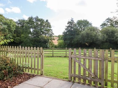 A wooden gate opening to a grassy yard with a wooden fence and trees in the background at Culver Court Cottage Venny Tedburn near Crediton