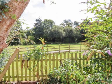A garden with plants and a wooden picket fence overlooking a grassy area with trees at Culver Court Cottage in Venny Tedburn near Crediton