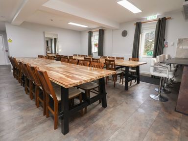 A dining area with wooden tables and chairs alongside a bar counter with white bar stools at The Bevan in Bontnewydd Gwynedd