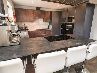 A kitchen with a black countertop island and white bar stools at The Bevan in Bontnewydd Gwynedd
