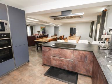 A kitchen with a stovetop island and wooden tables with chairs in the background at The Bevan in Bontnewydd Gwynedd