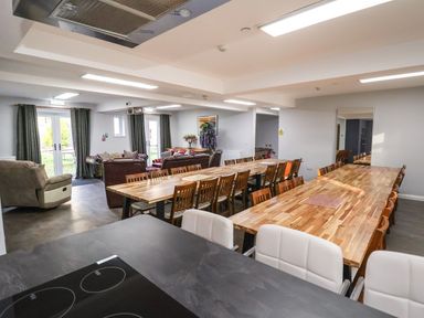 A dining area with wooden tables and chairs next to a living room with sofas and armchairs at The Bevan in Bontnewydd Gwynedd