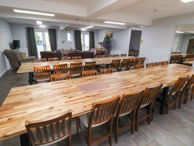 A communal dining area with wooden tables and chairs adjoining a lounge with sofas and armchairs at The Bevan in Bontnewydd Gwynedd