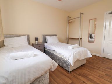 A bedroom with two single beds bedside table and lamp an open clothes rack and wall mirror at The Bevan in Bontnewydd Gwynedd