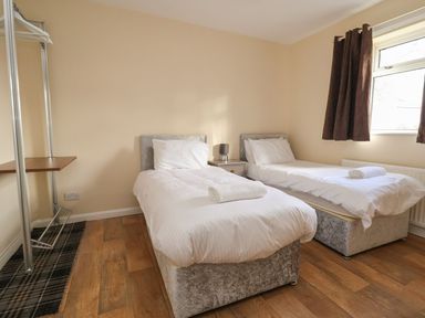 A bedroom with two single beds a nightstand a lamp a window and a small open closet at The Bevan in Bontnewydd Gwynedd