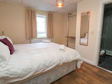 A bedroom with a bed white bedding and rolled towels next to a window and an open door to a bathroom at The Bevan in Bontnewydd Gwynedd