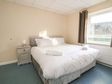 A bedroom with a double bed white bedding bedside table with lamp and window with curtains at The Bevan in Bontnewydd Gwynedd