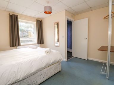 A bedroom with a bed, two rolled towels on the bed, a window with curtains, a wall mirror, an open door, and a clothing rack at The Bevan in Bontnewydd, Gwynedd
