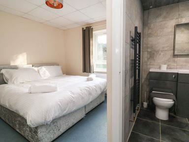 A bedroom with a double bed and white bedding next to a bathroom with a toilet and a black towel radiator at The Bevan in Bontnewydd Gwynedd