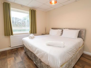 A bedroom with a large bed with white linens and towels near a window with green curtains at The Bevan in Bontnewydd Gwynedd