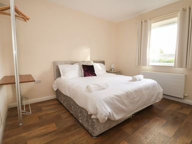 A bedroom with a double bed white bedding rolled towels wooden floor and a window with curtains at The Bevan in Bontnewydd Gwynedd