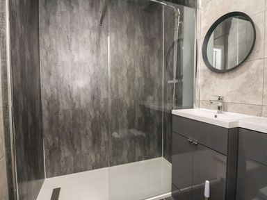 A bathroom with a glass shower enclosure a dark grey vanity unit with a sink and a round mirror at The Bevan in Bontnewydd Gwynedd
