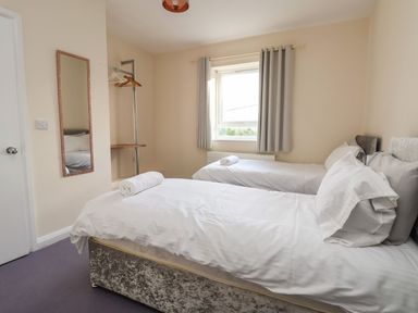 A bedroom with two single beds with white linens and rolled towels on top a window with curtains a wall mirror and a clothes rack at The Bevan in Bontnewydd Gwynedd