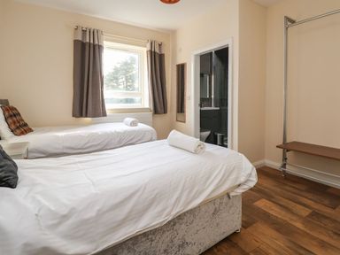 A bedroom with two single beds a window with curtains a mirror and an open door to a bathroom at The Bevan in Bontnewydd Gwynedd