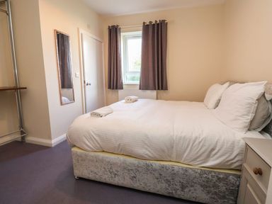 A bedroom with a bed, pillows, a window with curtains, a mirror on the wall, and a bedside table at The Bevan in Bontnewydd Gwynedd
