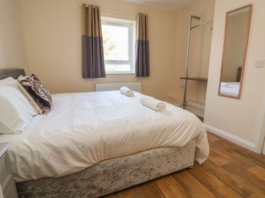 A bedroom with a double bed two rolled towels on the bed a window with curtains a standing mirror and an open closet at The Bevan in Bontnewydd Gwynedd