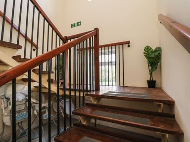 A staircase with wooden steps and black railings with a fire exit sign and a potted plant on the landing at The Bevan in Bontnewydd Gwynedd