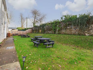 An outdoor area with picnic tables on grass next to a stone wall and a building at The Bevan in Bontnewydd Gwynedd