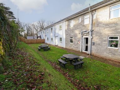 A grassy backyard with picnic tables and a row of residential buildings in the background at The Bevan in Bontnewydd Gwynedd