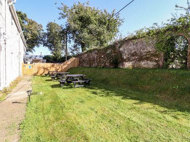 A grassy outdoor area with wooden picnic tables along a wall and a pathway beside a building at The Bevan in Bontnewydd Gwynedd