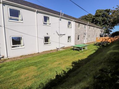An outdoor grassy area with a ping pong table and picnic benches next to a two story building with windows at The Bevan in Bontnewydd Gwynedd