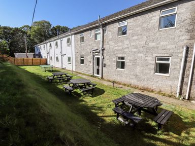 A grassy outdoor area with wooden picnic tables next to a stone and white building under a clear sky at The Bevan in Bontnewydd Gwynedd