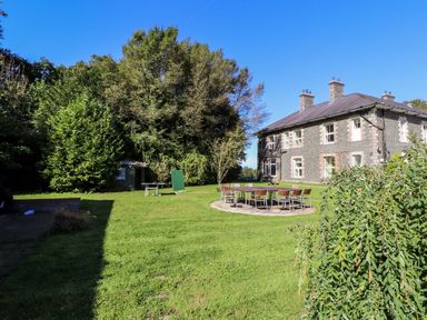An outdoor garden with a round table and chairs near a stone house with multiple chimneys at The Bevan in Bontnewydd Gwynedd