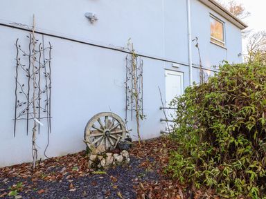 An exterior view of a building with a white door a window and a garden area with a wooden wagon wheel leaning against the wall at The Bevan in Bontnewydd Gwynedd