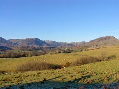 A rural landscape with grassy fields sheep scattered and hills under a clear blue sky at The Bevan in Bontnewydd Gwynedd