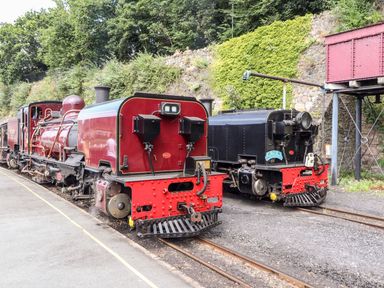Two vintage steam locomotives on railway tracks near a stone wall and greenery at The Bevan in Bontnewydd Gwynedd