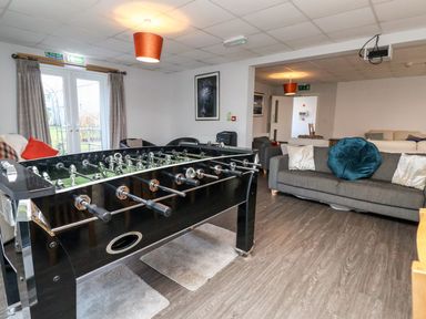 A room with a foosball table, gray couches with pillows, chairs, and a door with curtains at Cadwaladr in Bontnewydd near Caernarfon