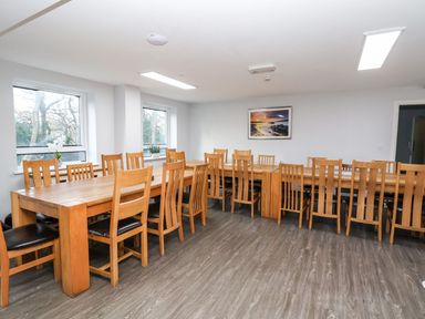A dining room with two long wooden tables and multiple wooden chairs and windows on one wall at Cadwaladr in Bontnewydd near Caernarfon