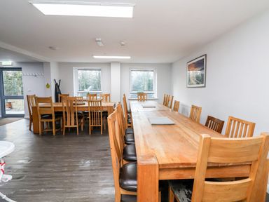 A dining room with wooden tables and chairs and two windows at Cadwaladr in Bontnewydd near Caernarfon