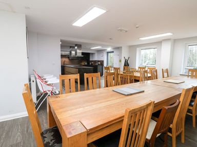 A dining area with wooden tables and chairs adjacent to a kitchen with stainless steel appliances at Cadwaladr in Bontnewydd near Caernarfon