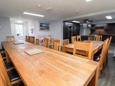 A dining area with two wooden tables and chairs near a kitchen with dark cabinets at Cadwaladr in Bontnewydd near Caernarfon