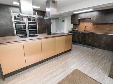 A kitchen with an island having cooktops and ovens built into dark cabinets at Cadwaladr in Bontnewydd near Caernarfon