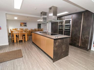 A kitchen with an island and built-in ovens and wooden dining tables with chairs at Cadwaladr in Bontnewydd near Caernarfon