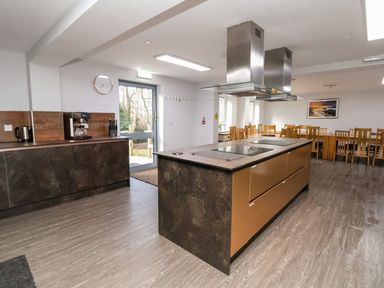 A kitchen with an island, stove hoods, a coffee machine, kettle, knives, and wooden chairs at Cadwaladr in Bontnewydd near Caernarfon