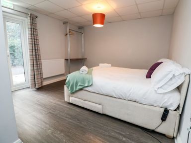 A bedroom with a single bed a blanket towels an open clothes rack a door with curtains and a ceiling light at Cadwaladr in Bontnewydd near Caernarfon