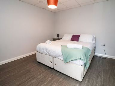 A bedroom with a bed white bedding a green blanket and a purple pillow on wooden floor at Cadwaladr Bontnewydd near Caernarfon