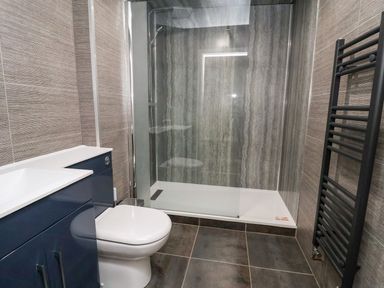 A bathroom with a toilet blue cabinet a walk in shower and a black towel radiator at Cadwaladr in Bontnewydd near Caernarfon