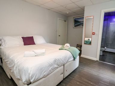 A bedroom with a bed with white linens and a purple pillow a mirror on the wall and an open door to a bathroom at Cadwaladr in Bontnewydd near Caernarfon